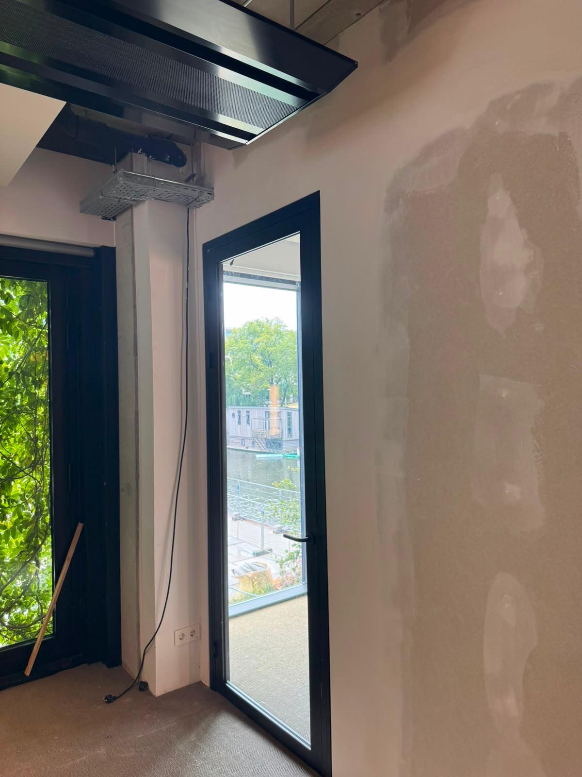 Afgewerkte gladde wand in een kantoorruimte met zwart kozijn en uitzicht op een gracht met woonboten