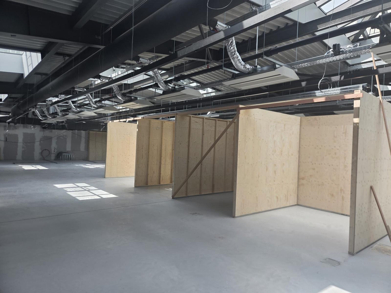 Bedrijfshal met plywood cabines, stalen liggers, ventilatiekanalen en verlichtingsarmaturen