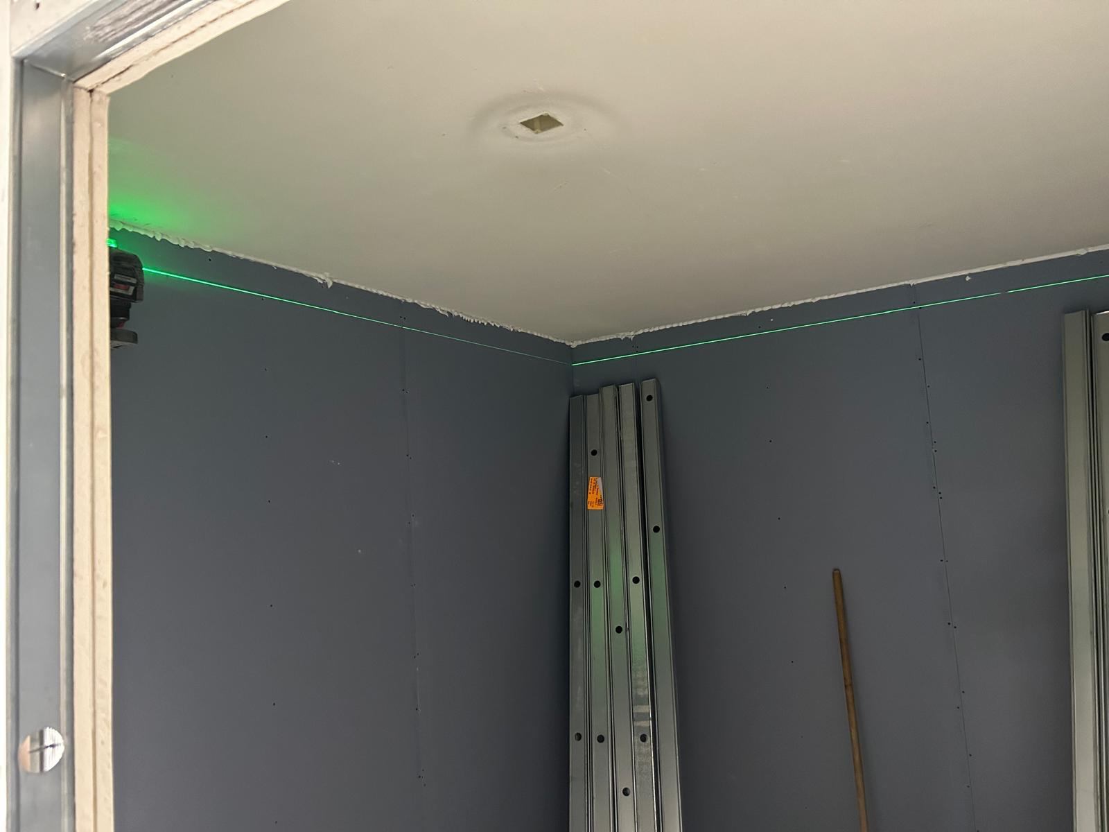 Grijze geluidwerende wanden met groene laserlijn langs het plafond en een bundel metalstud profielen in de hoek