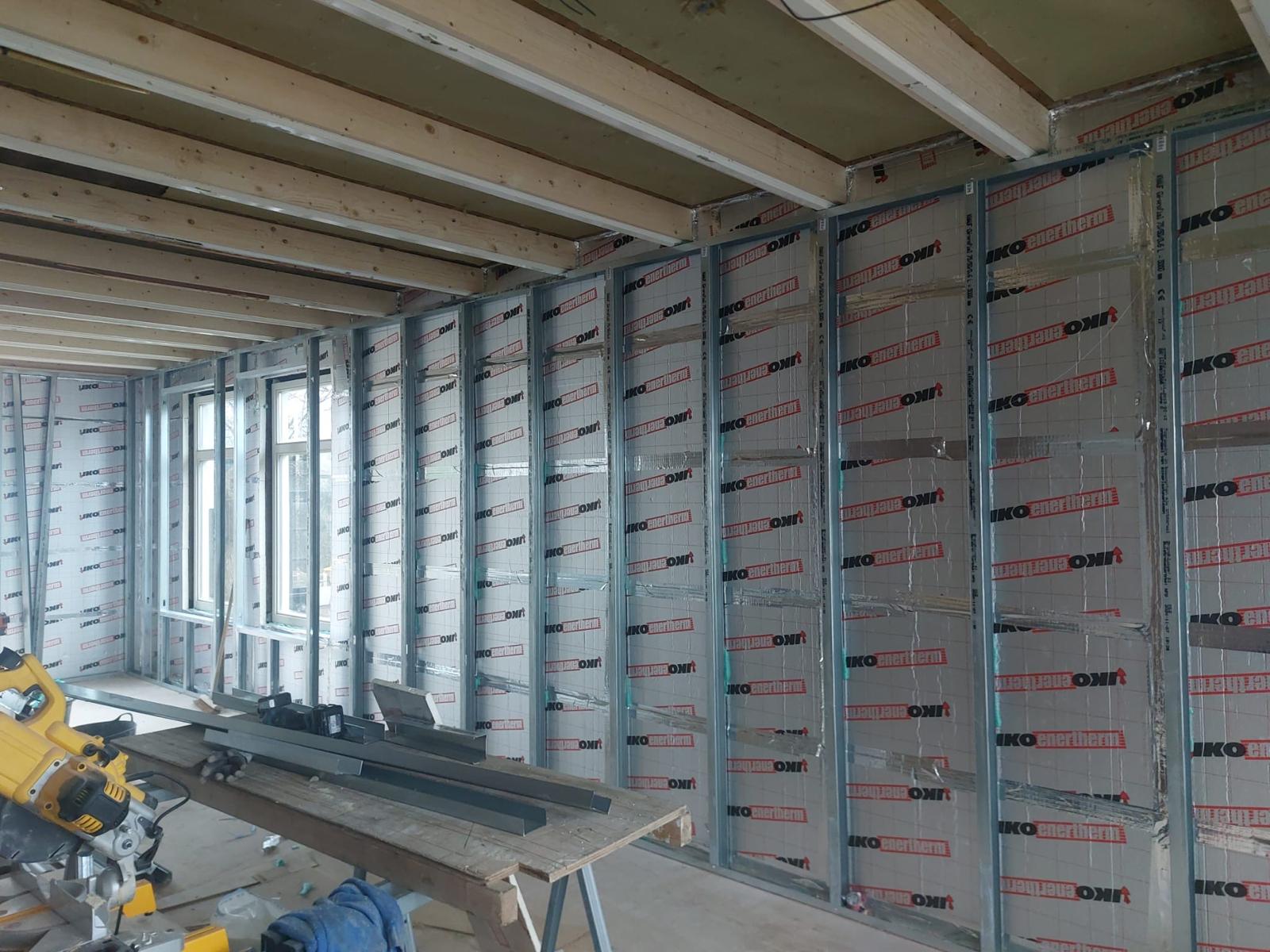 Metalstud voorzetwand met verzinkte profielen en IKO enertherm PIR-platen langs een raampartij, met houten balklaag erboven