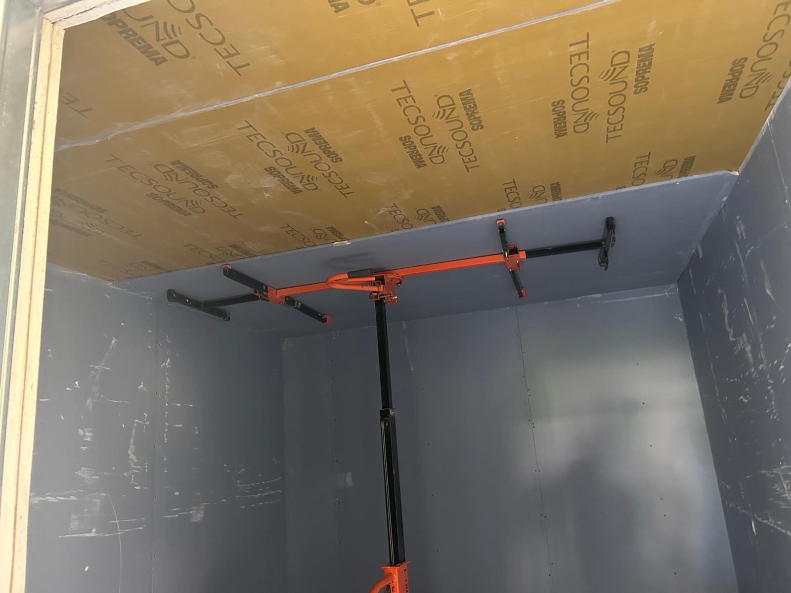 Plafond met Tecsound membraan, gemonteerd met een oranje plafondlift in een grijs afgewerkte ruimte