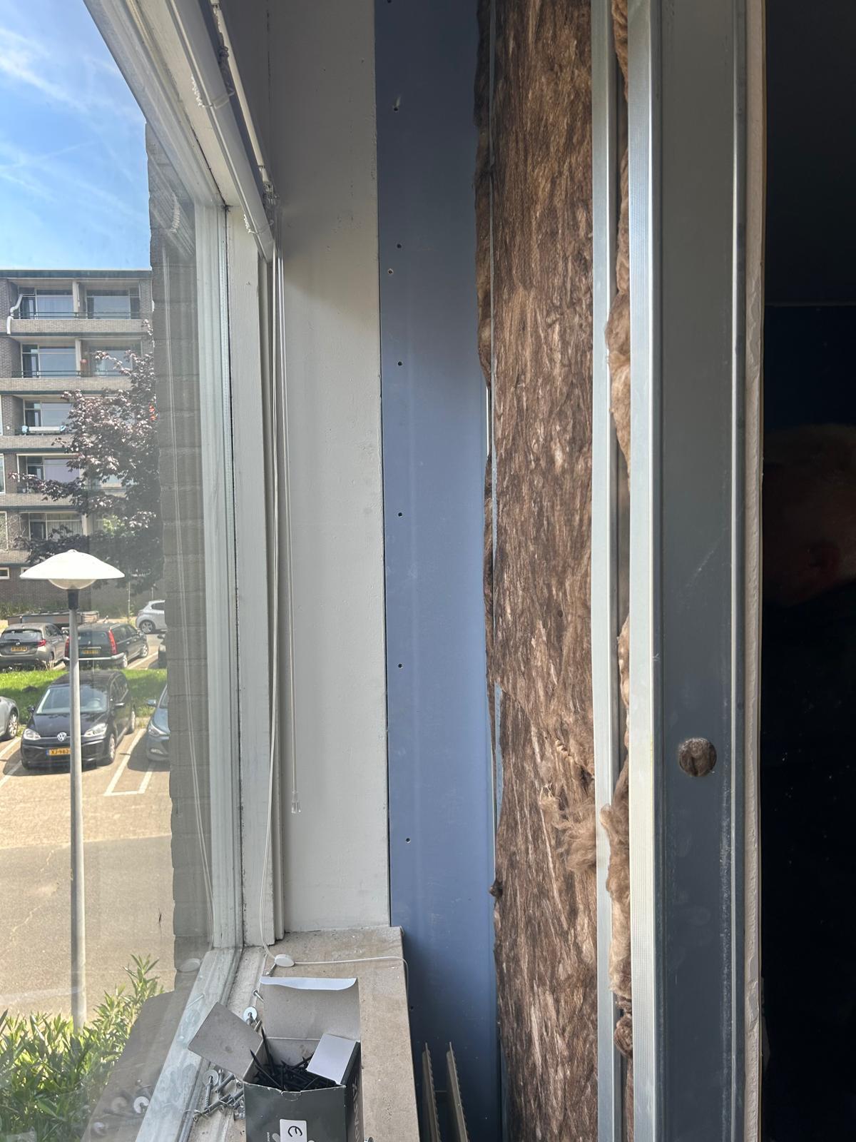 Raamaansluiting in een appartement met blauwe gipsplaat en minerale wol in de spouw, uitzicht op flatgebouwen