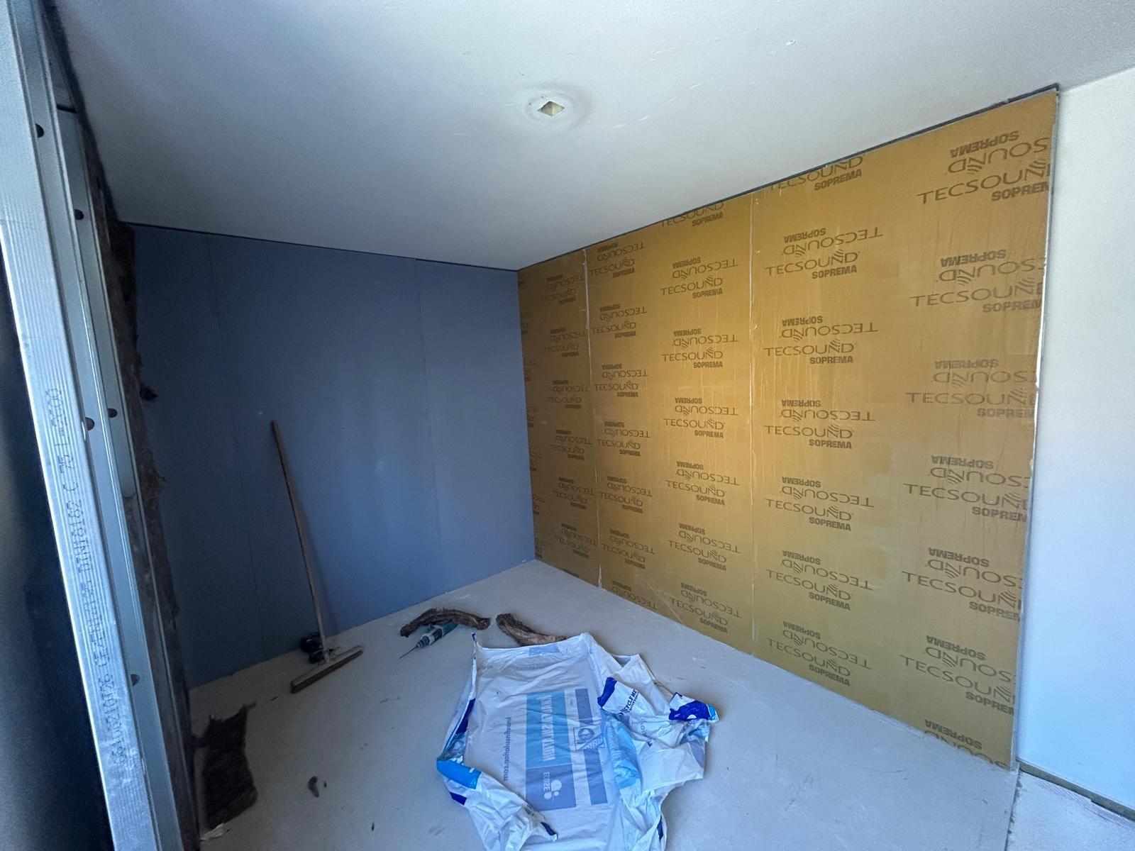 Ruimte met een wand volledig bekleed met okerkleurig Tecsound Soprema membraan naast een afgewerkte grijze dB-wand