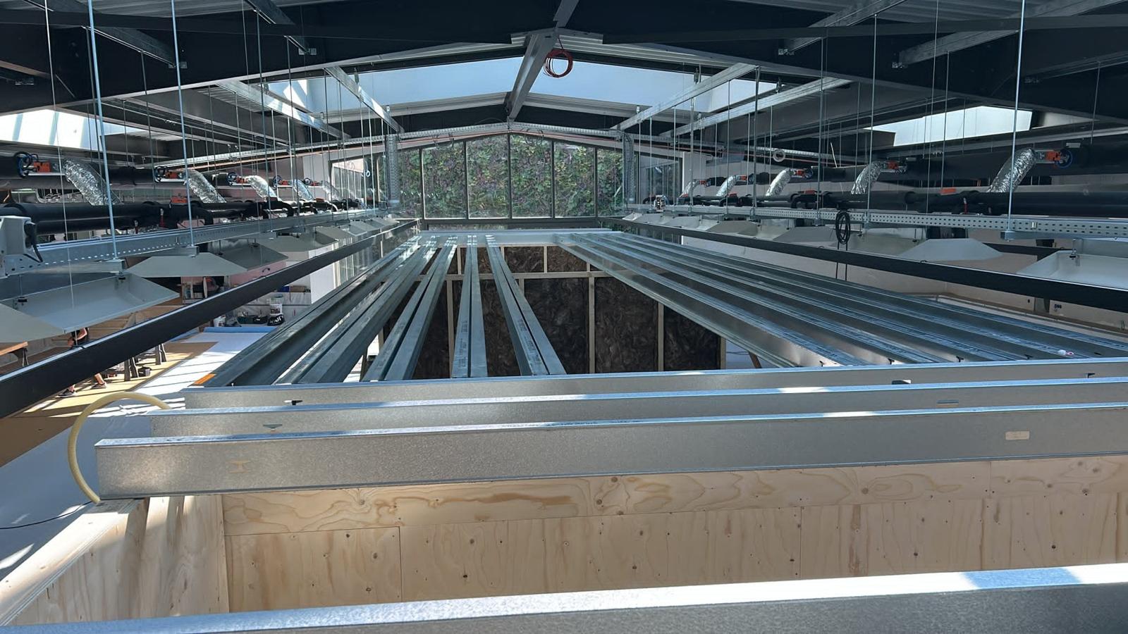 Bedrijfshal met stalen metalstud profielen over een vide, glazen daklichten en zichtbaar ventilatiewerk
