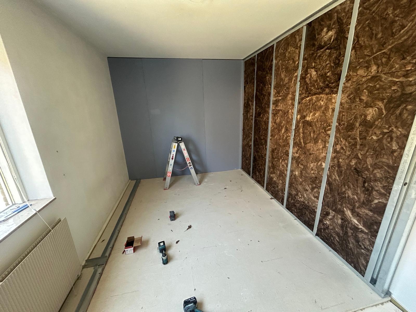 Kamer met half gemonteerde voorzetwand, grijze gipsplaten links en minerale wol tussen de stalen regels rechts